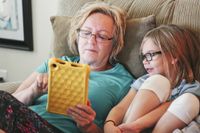 A grandmother and granddaughter sitting on a couch looking at a tablet.